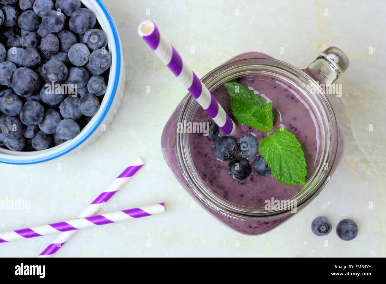 Blueberry smoothie with mint in mason jar glass with straw. Above view on white marble. Stock Photo