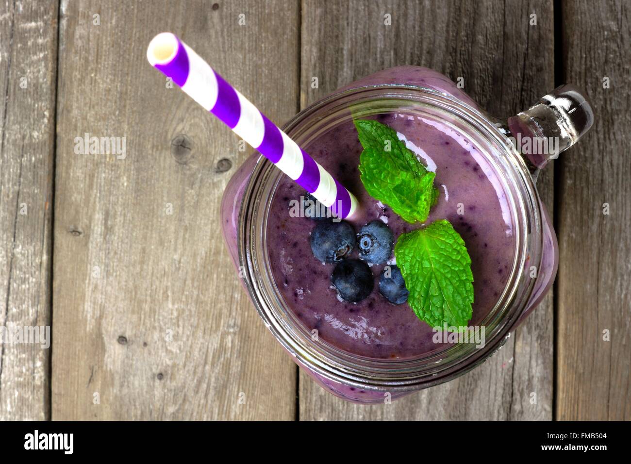 Blueberry smoothie with mint in mason jar mug with straw. Above view on wood. Stock Photo