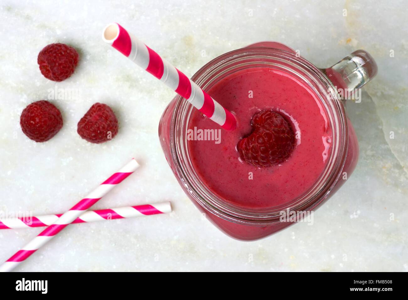 Pink raspberry smoothie in a mason jar, overhead view with straws on white marble background Stock Photo