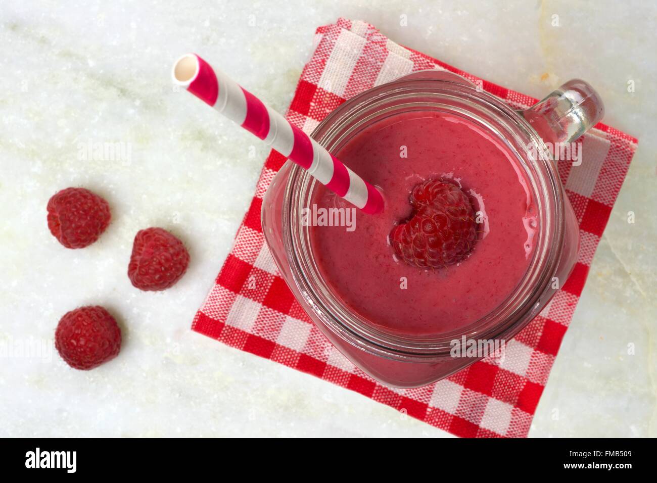 Pink raspberry smoothie in a mason jar with straw, overhead view with checked cloth on white marble background Stock Photo