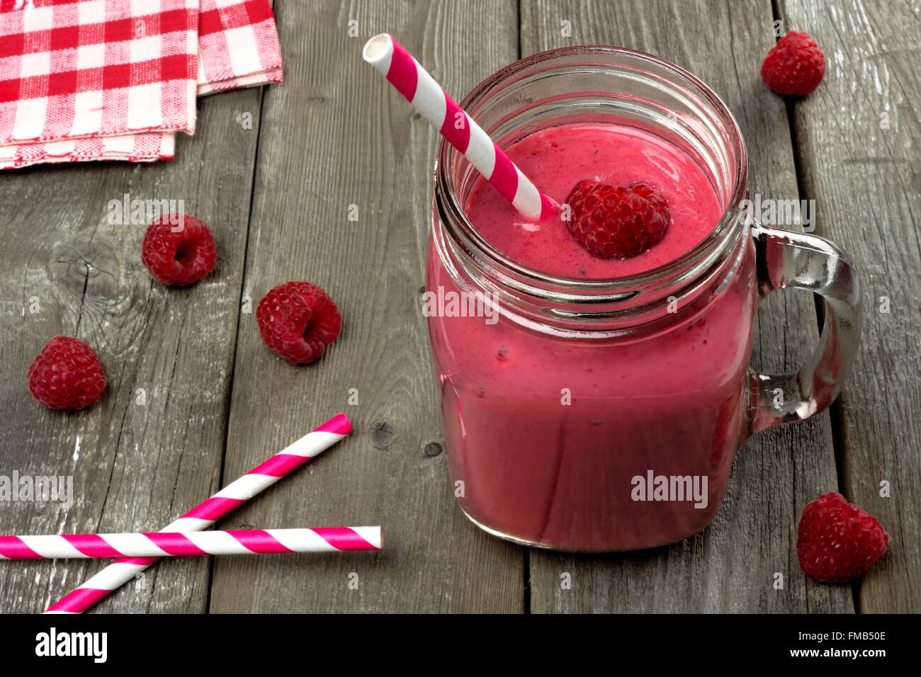 Pink raspberry smoothie in a mason jar with straws on a rustic wood background Stock Photo