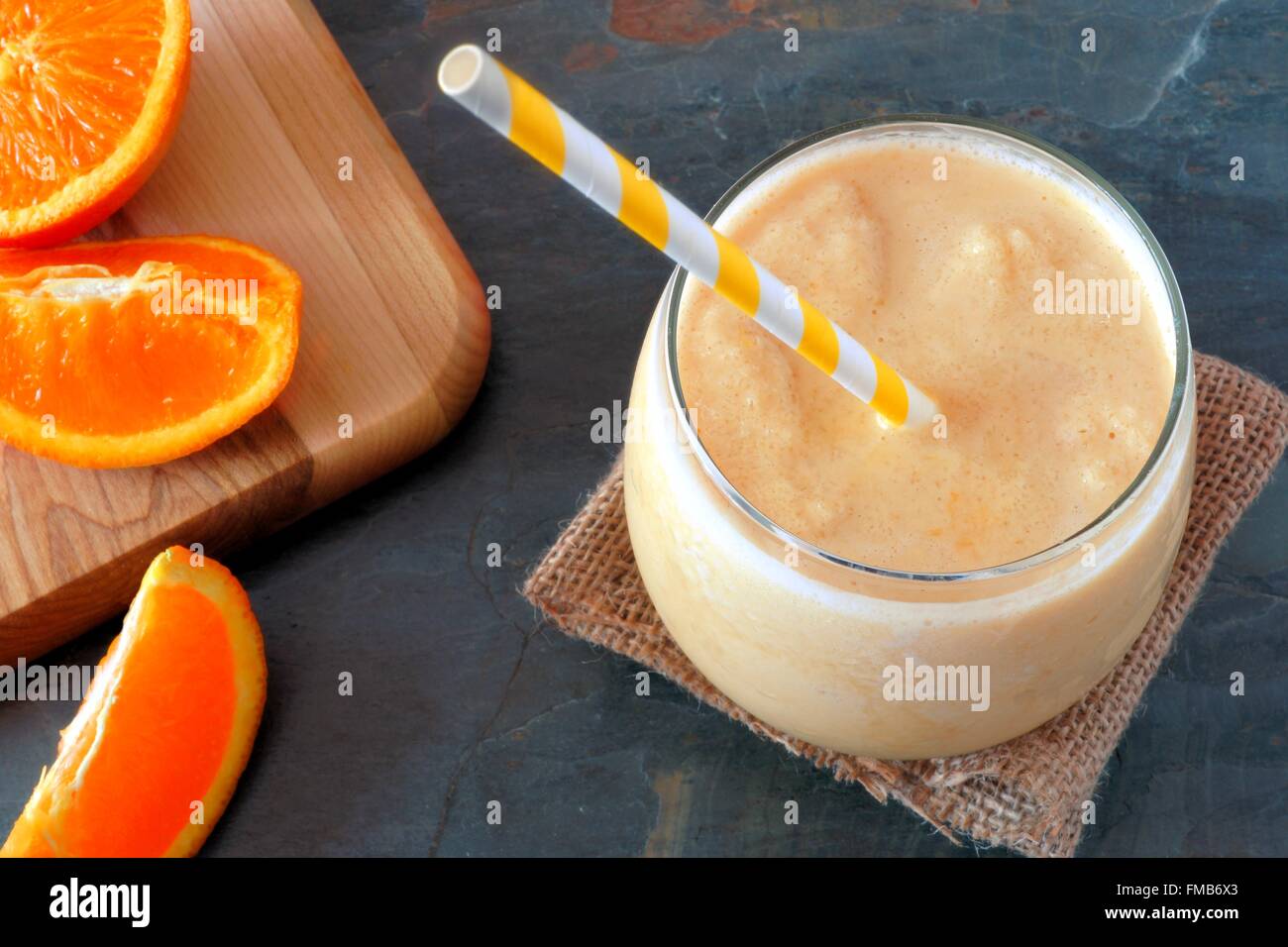 Healthy orange smoothie in a glass with striped straw and fresh fruit slices, downward view on slate Stock Photo