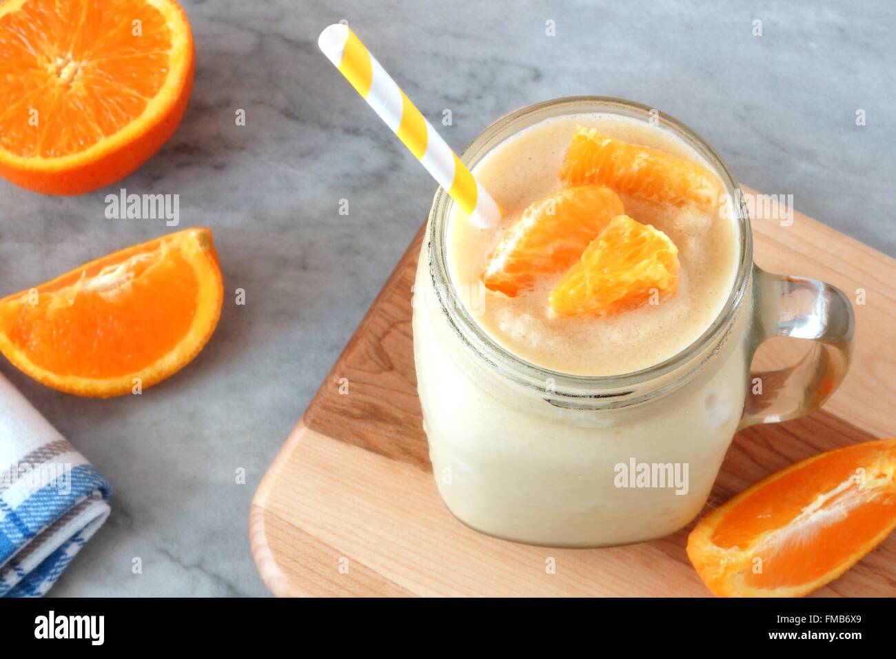 Orange fruit smoothie in a mason jar glass with straw resting on wood with fresh orange slices over a granite background Stock Photo