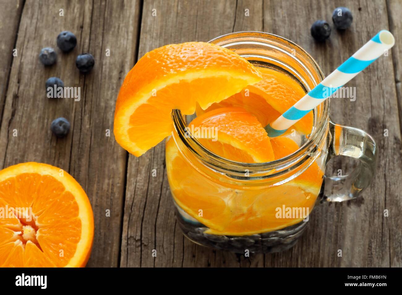 Detox water with oranges and blueberries in a mason jar with straw. Downward view on wood. Stock Photo