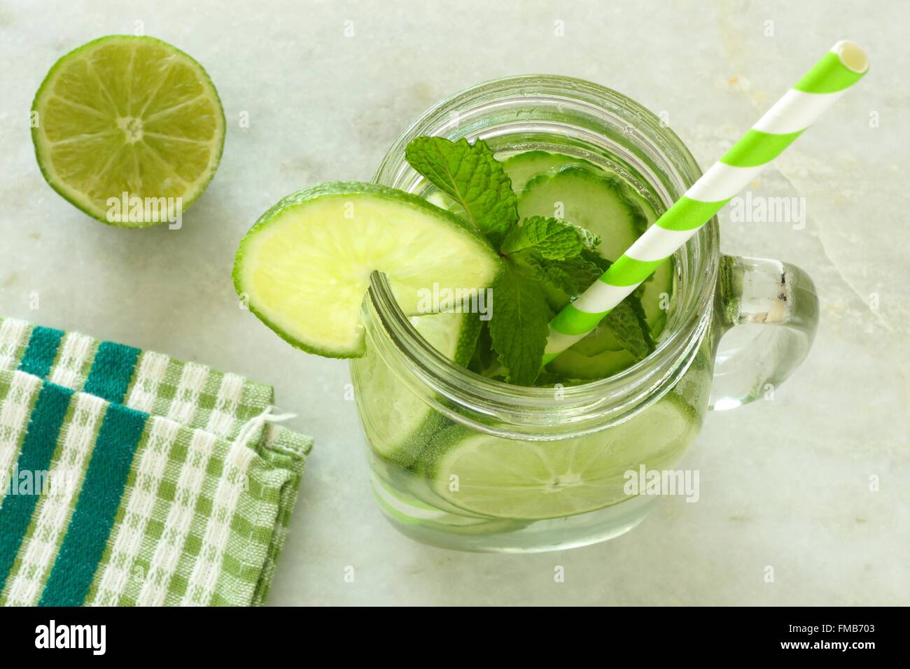 Detox water with lime and cucumbers in a mason jar with straw. Downward view on white marble. Stock Photo
