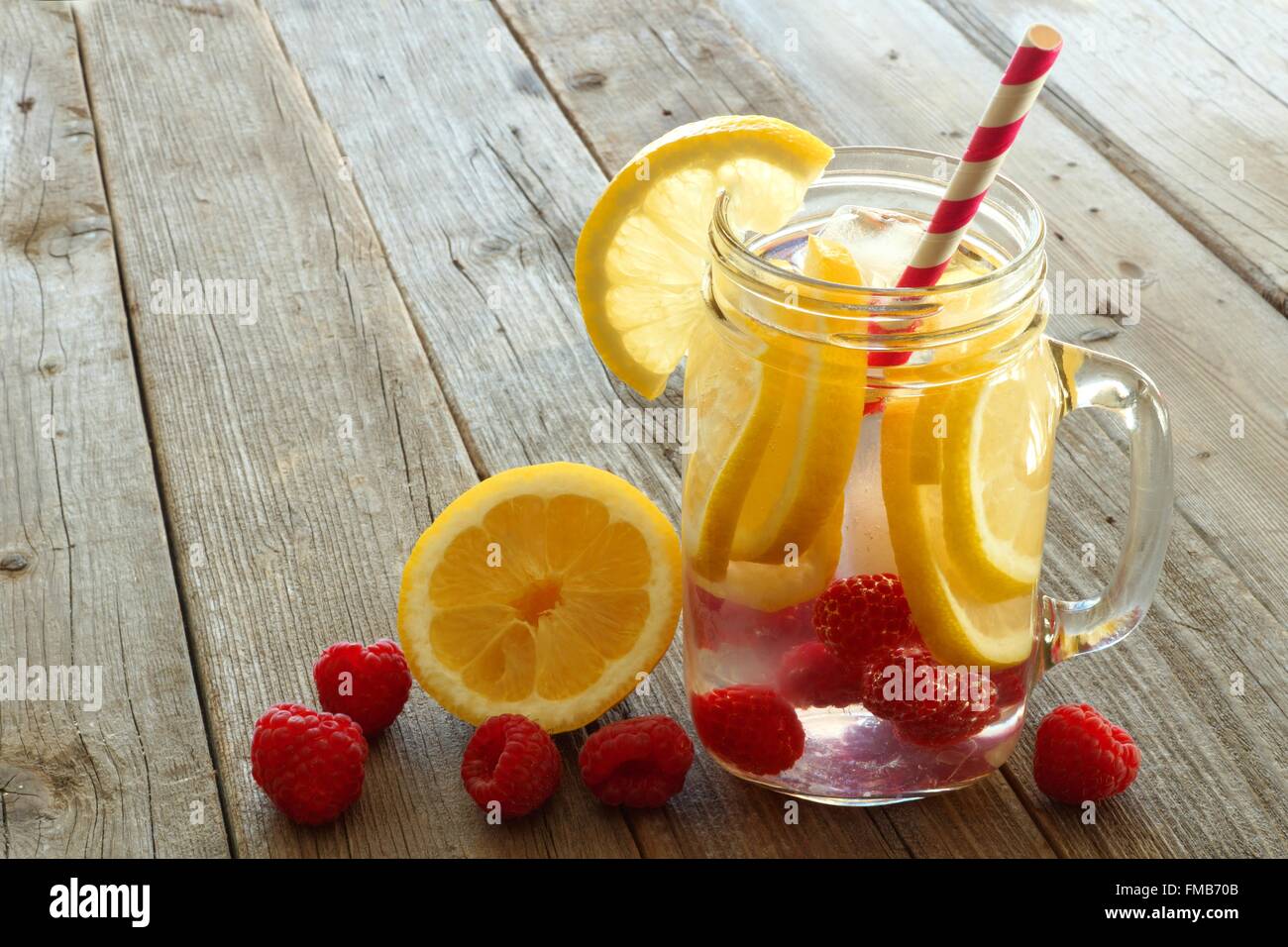 Vitamin water with lemon and raspberries in a jar with straw against a wood background Stock Photo