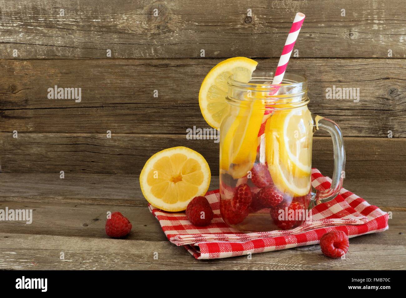 Detox water with lemon and raspberries in a jar with straw and cloth against a wood background Stock Photo