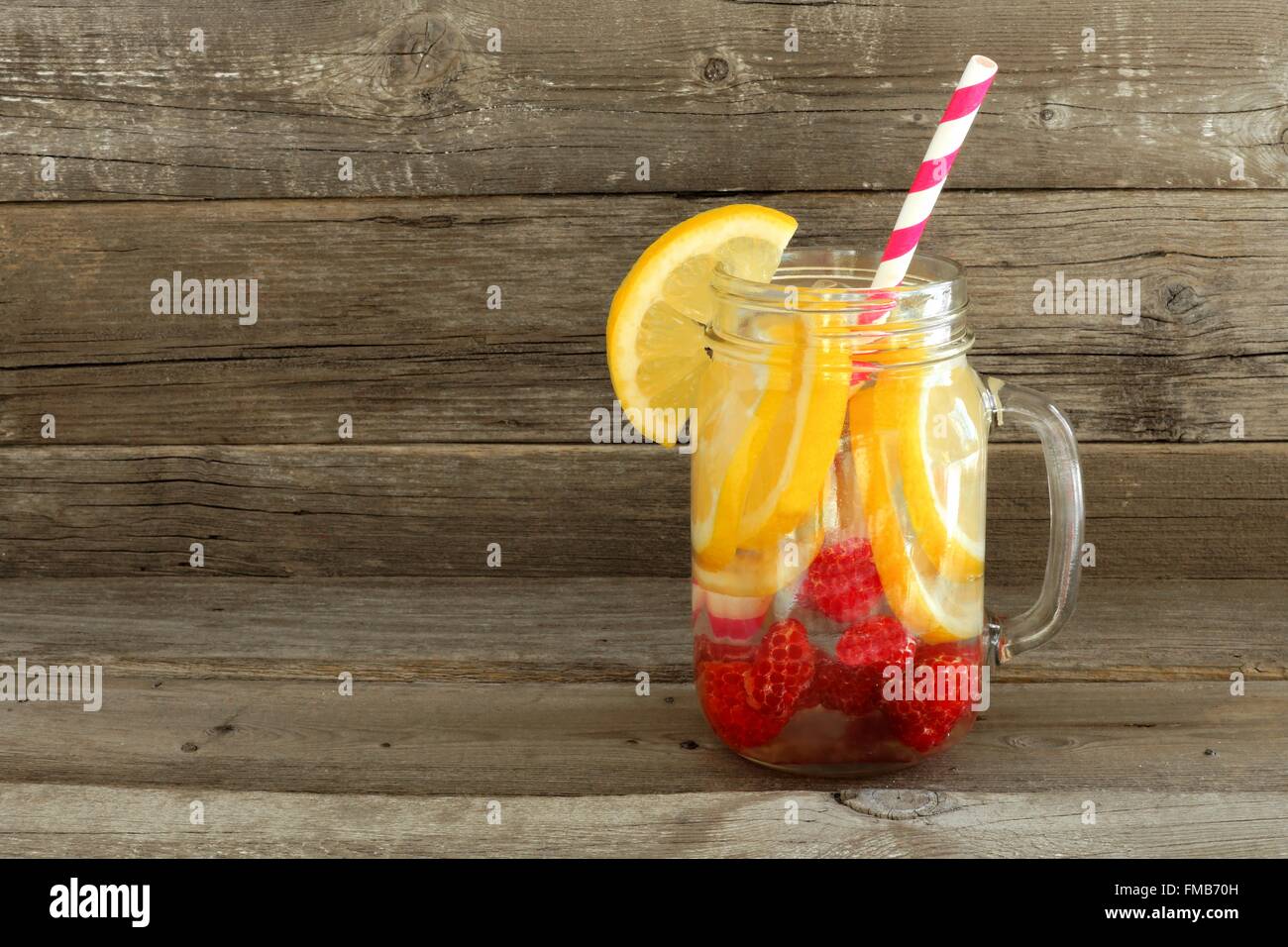 Detox water with lemon and raspberries in a mason jar with straw against a wood background Stock Photo