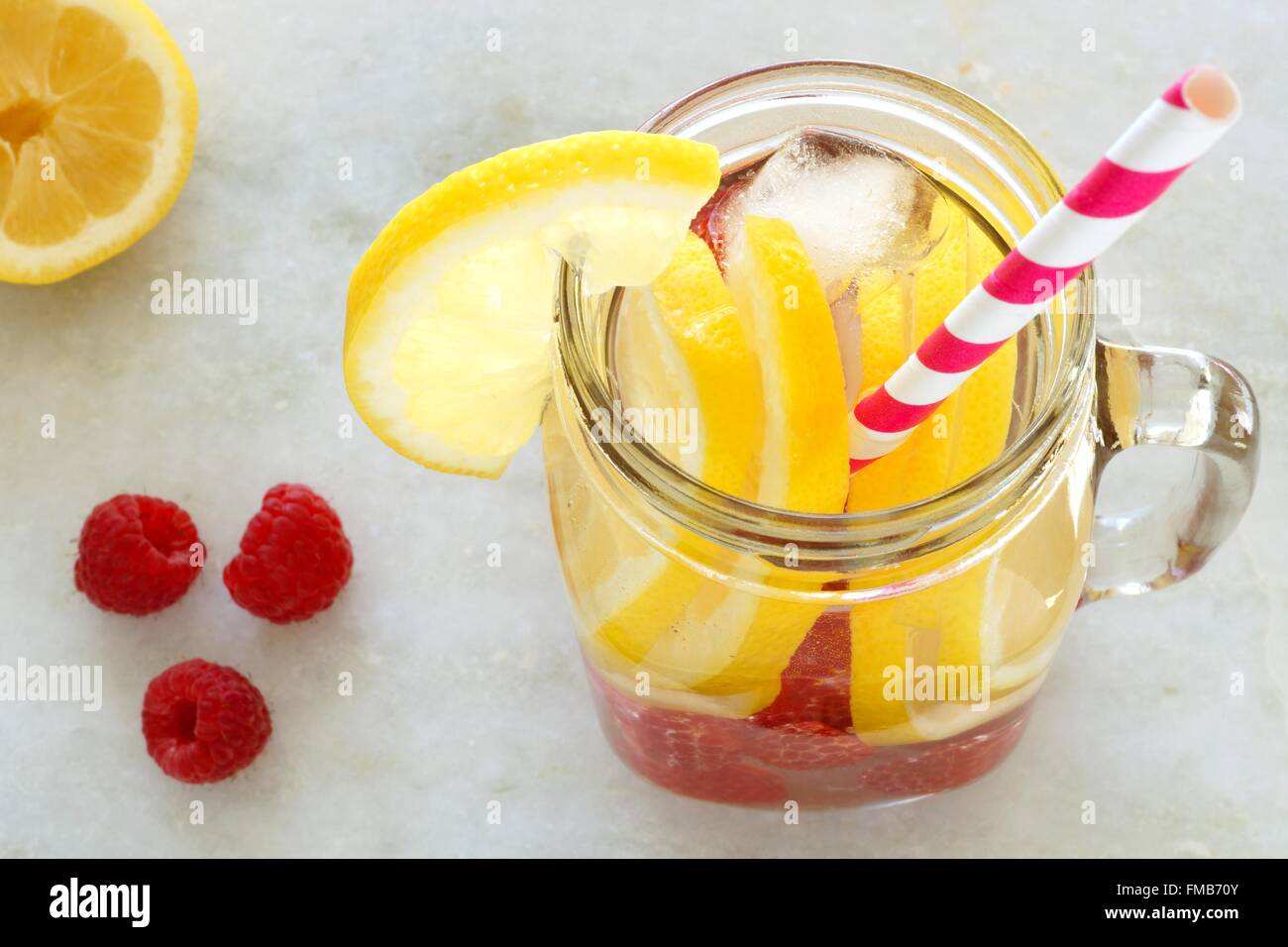 Spa water with lemon and raspberries in a mason jar with straw. Downward view on white marble. Stock Photo