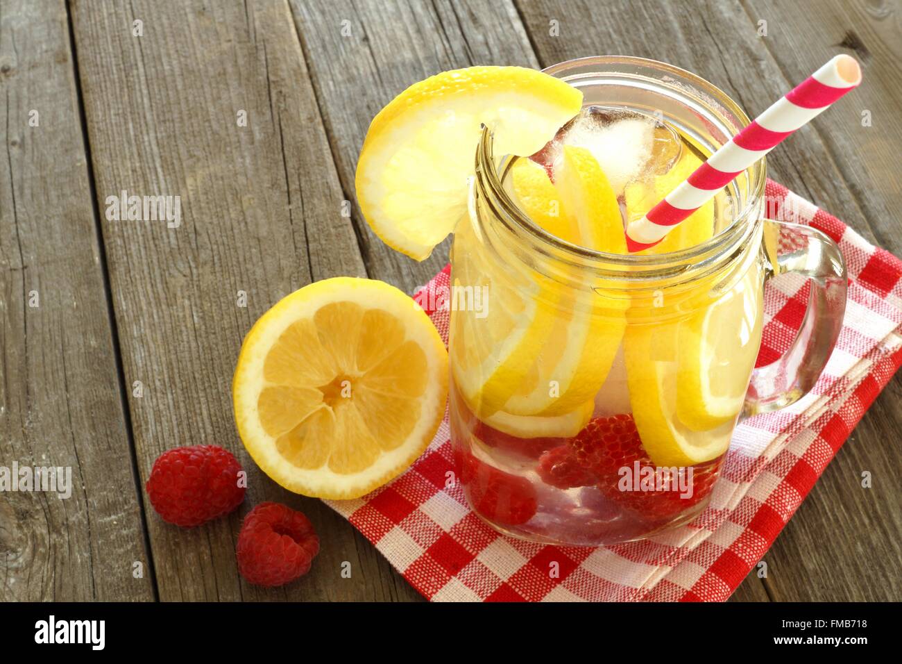 Detox water with lemon and raspberries in a mason jar with straw. Downward view on wood. Stock Photo