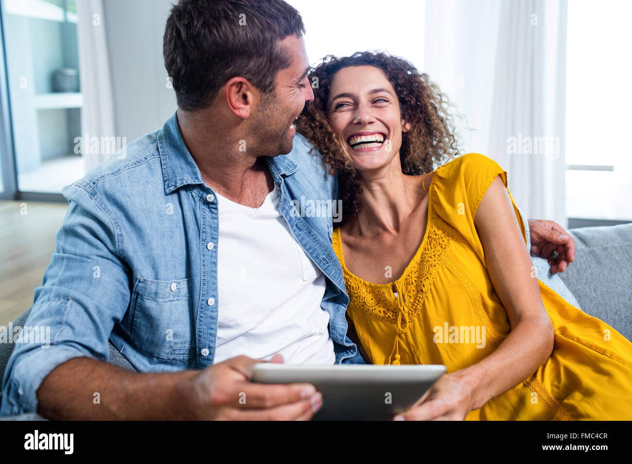 Happy couple using a digital tablet on sofa Stock Photo - Alamy