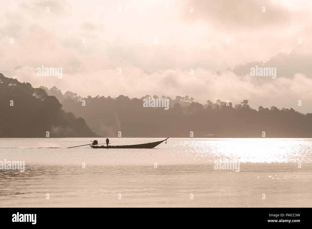Sihouetted sailing boat and man in distance during the morning on the big dam called 'Ratchaprapha' or 'Chiew Lan' in Suratthani Stock Photo
