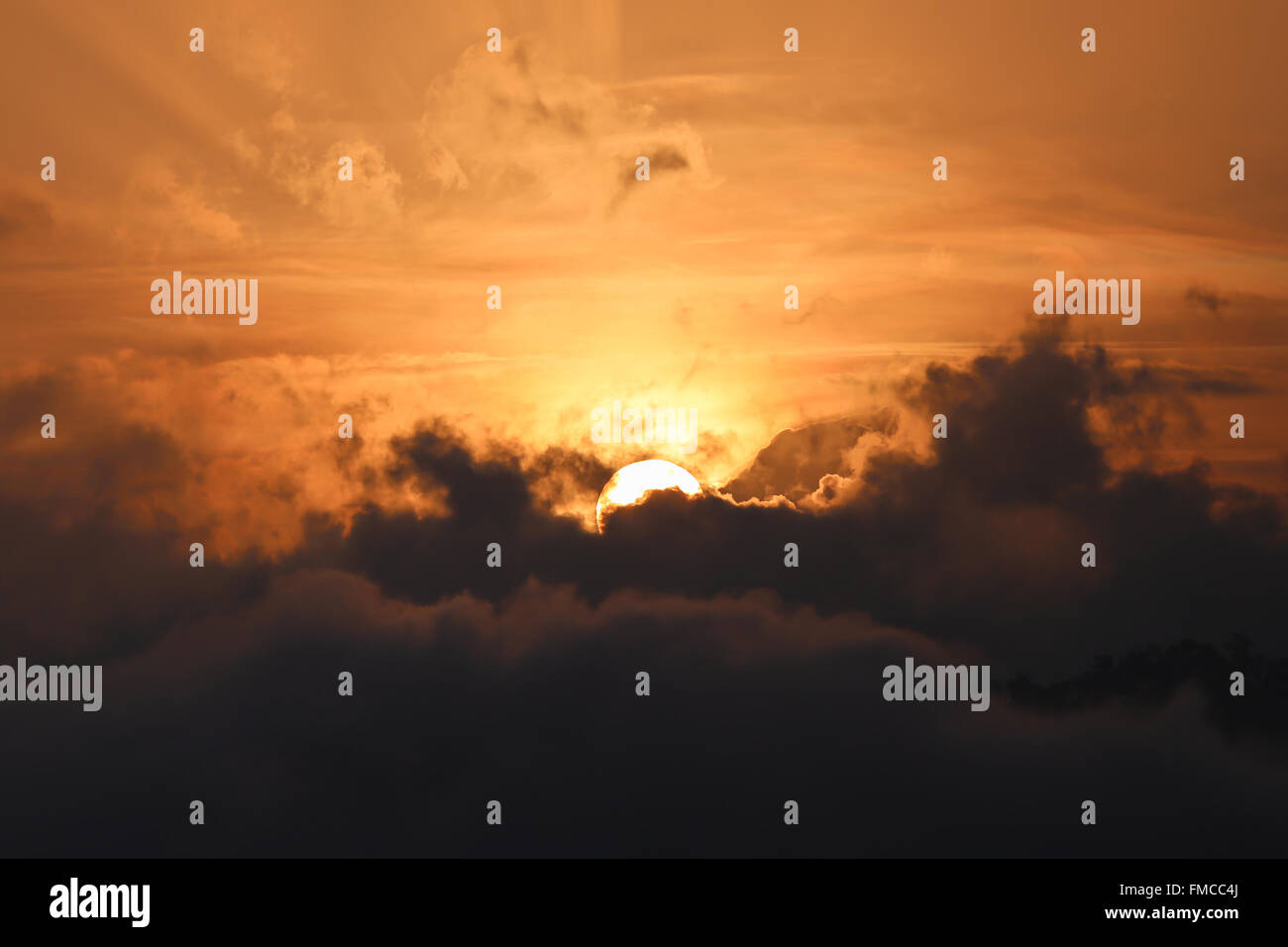 Partial of sun appears from dark cloud in the morning with golden sky Stock Photo