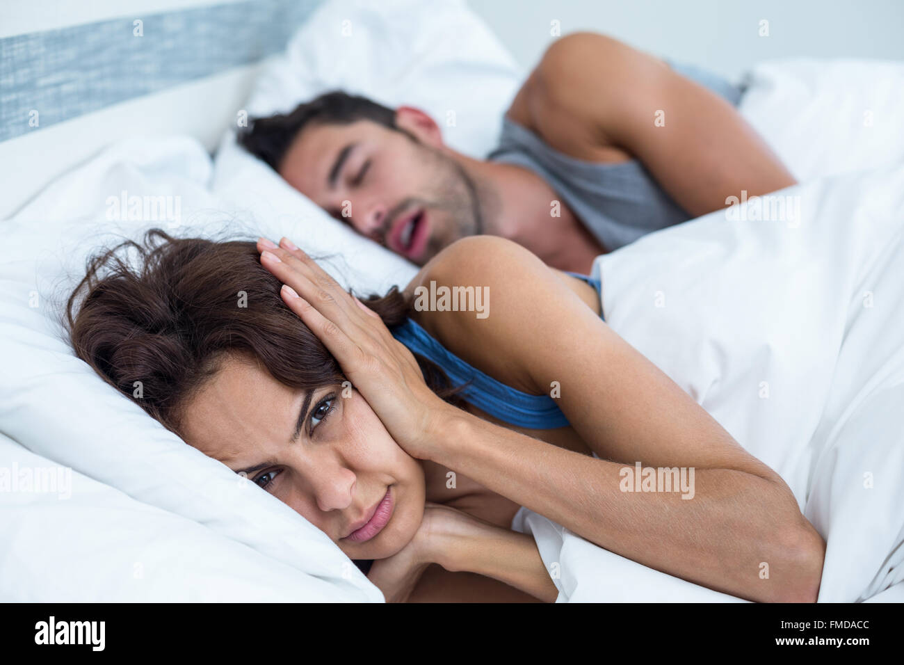 Woman blocking ears with hands while man snoring on bed Stock Photo