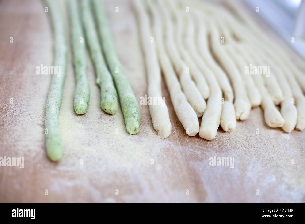 Round strips of green and white pasta dough on a wooden surface dusted with semolina flour Stock