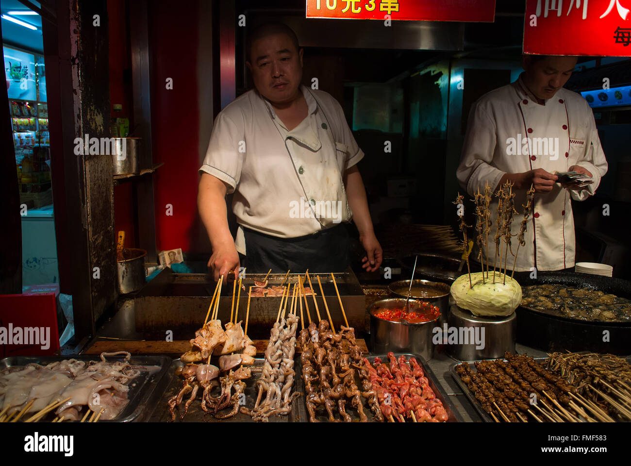 Cooks grilling local fast food delicacies of scorpions, locusts, starfish, squid and other in the busy night markets Stock Photo
