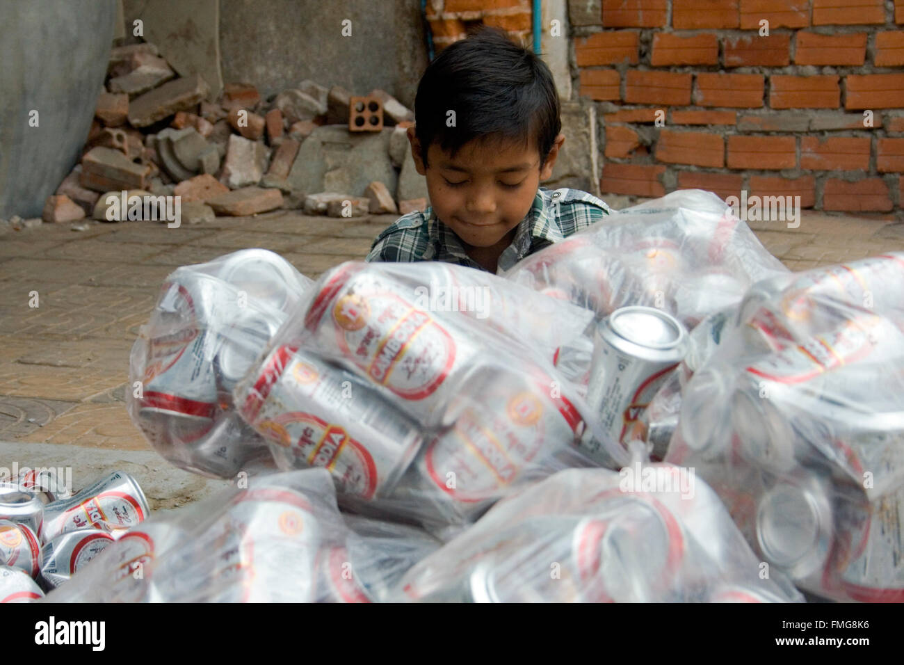 A young boy who is a scavenger is smashing aluminum cans on a city street in Kampong Cham, Cambodia. Stock Photo