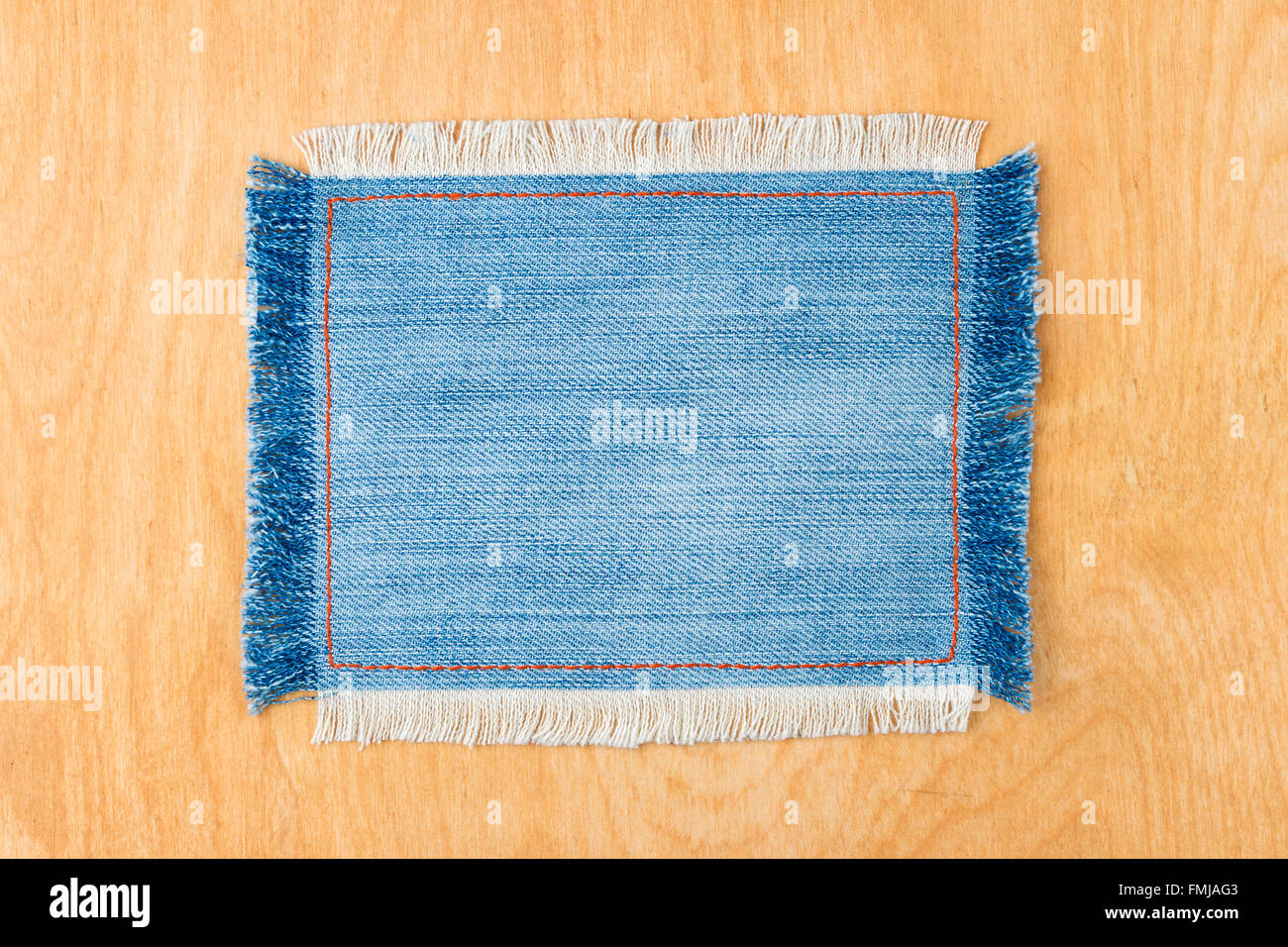 Frame for the text from a blue jeans fabric with the stitched lines of an orange thread and fringed, on a wooden background Stock Photo