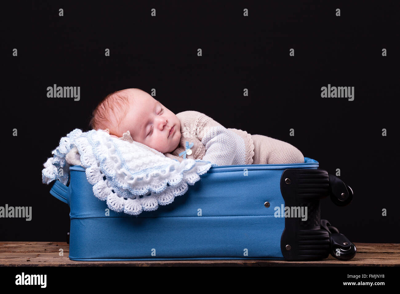 Newborn baby sleeping inside trolley bag against black background Stock