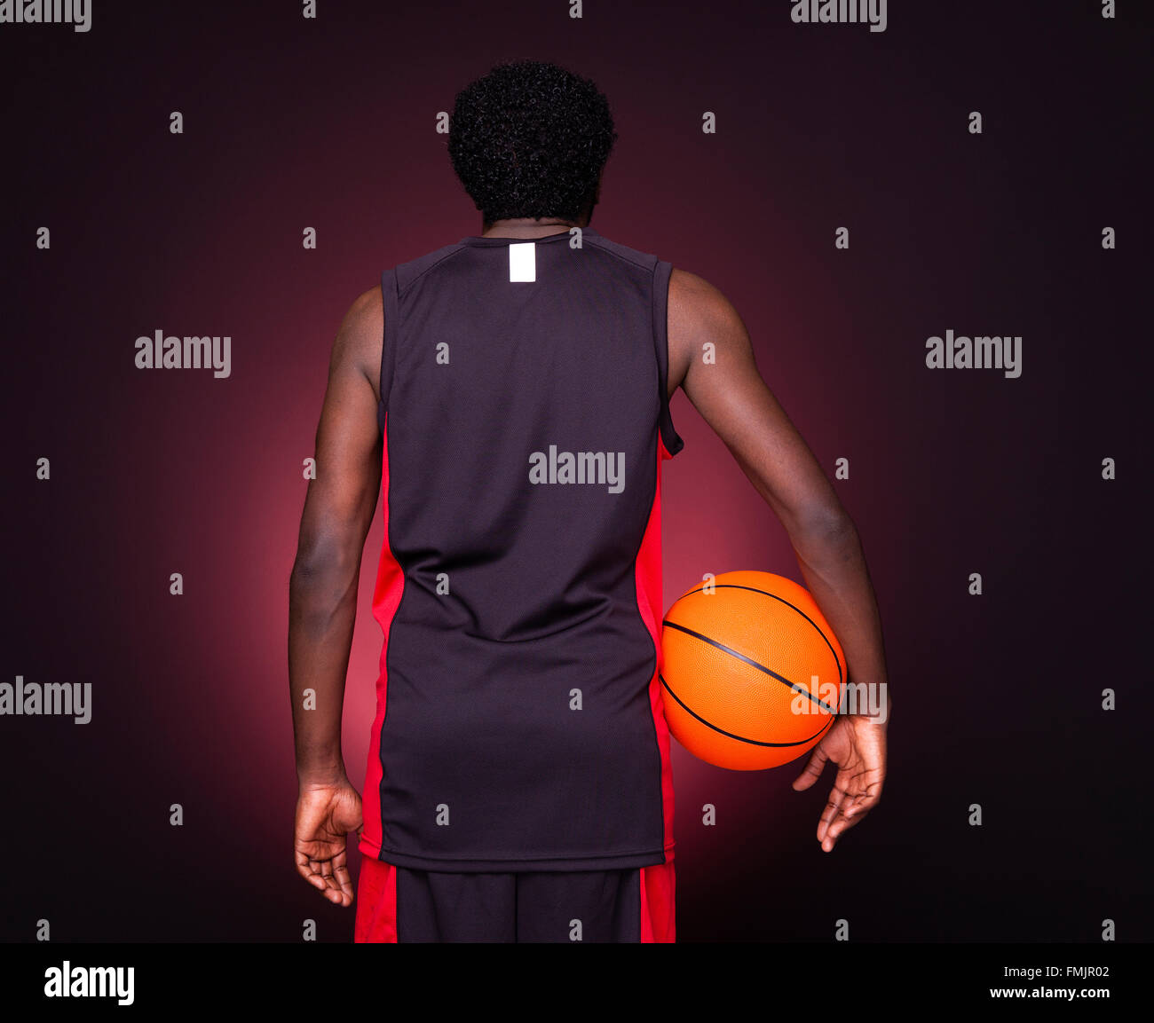 Back view of a basketball player holding a basketball against dark