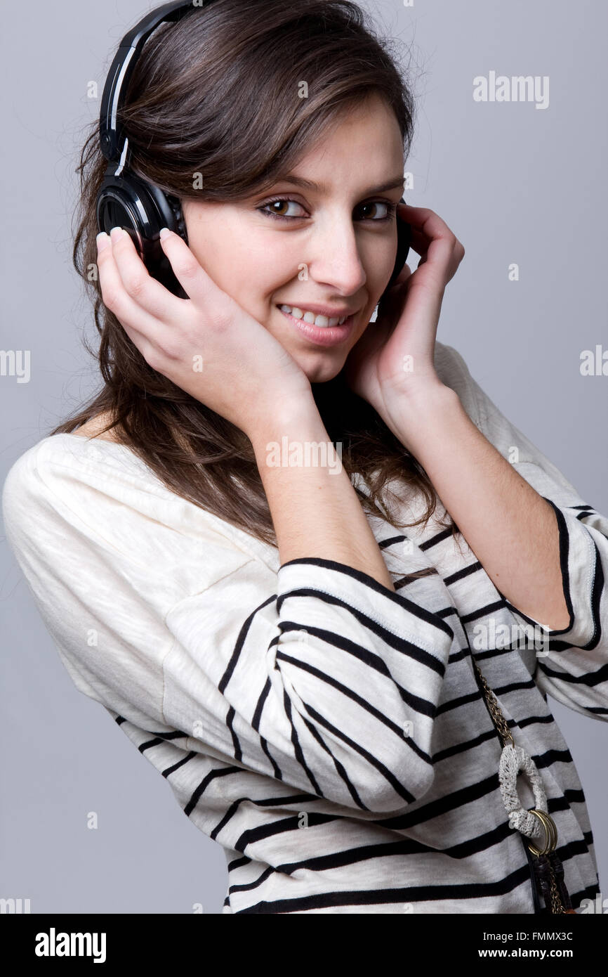 Smiling young woman listening to music over gray background Stock Photo ...