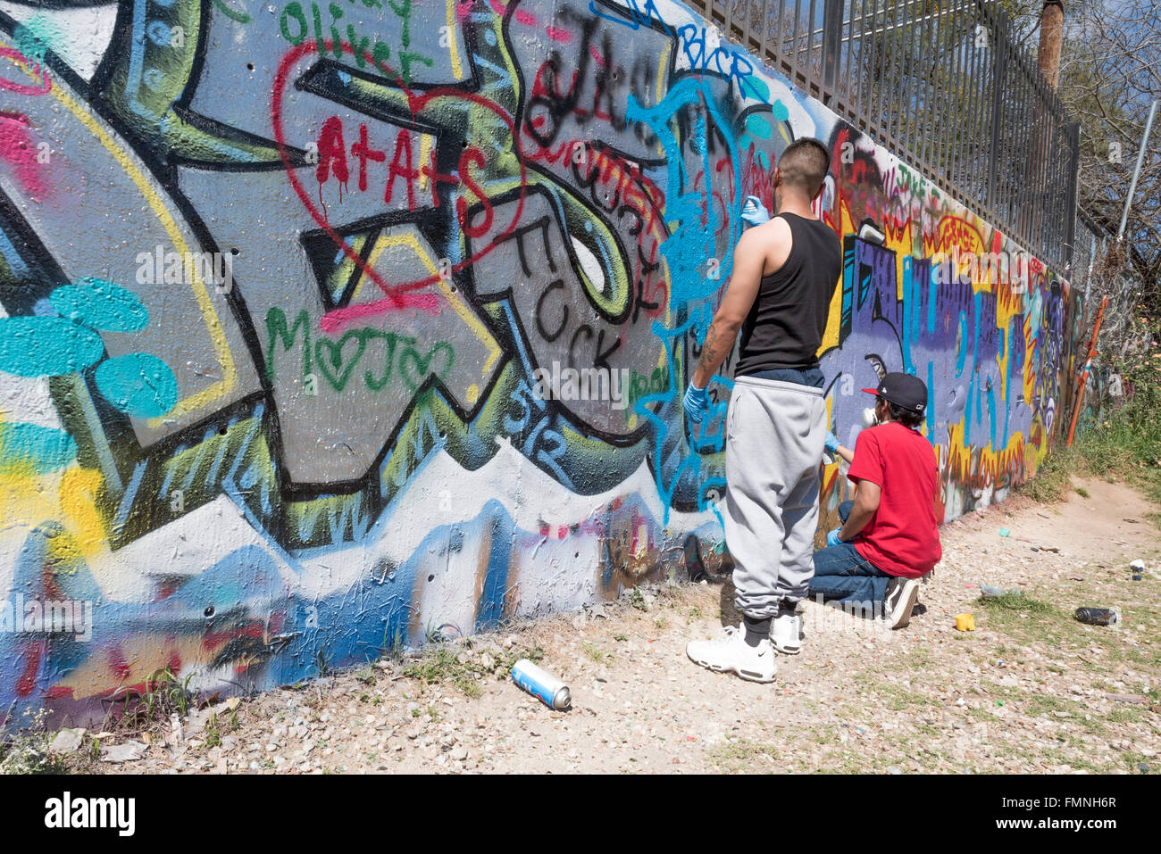 Graffiti artists spray paining on a wall at the Austin Graffiti Park