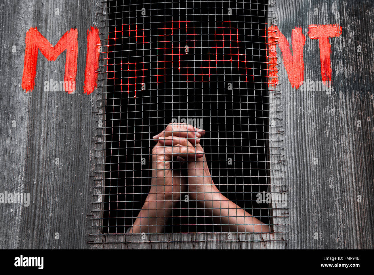 Hands behind bars, graffiti reading migrant, support for refugees Stock Photo
