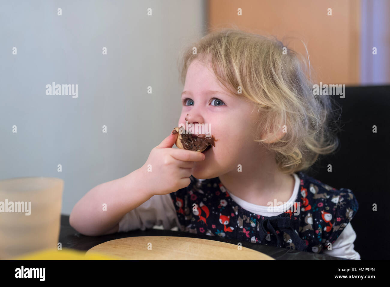 Little blonde girl biting into a bun with chocolate spread, Germany Stock Photo