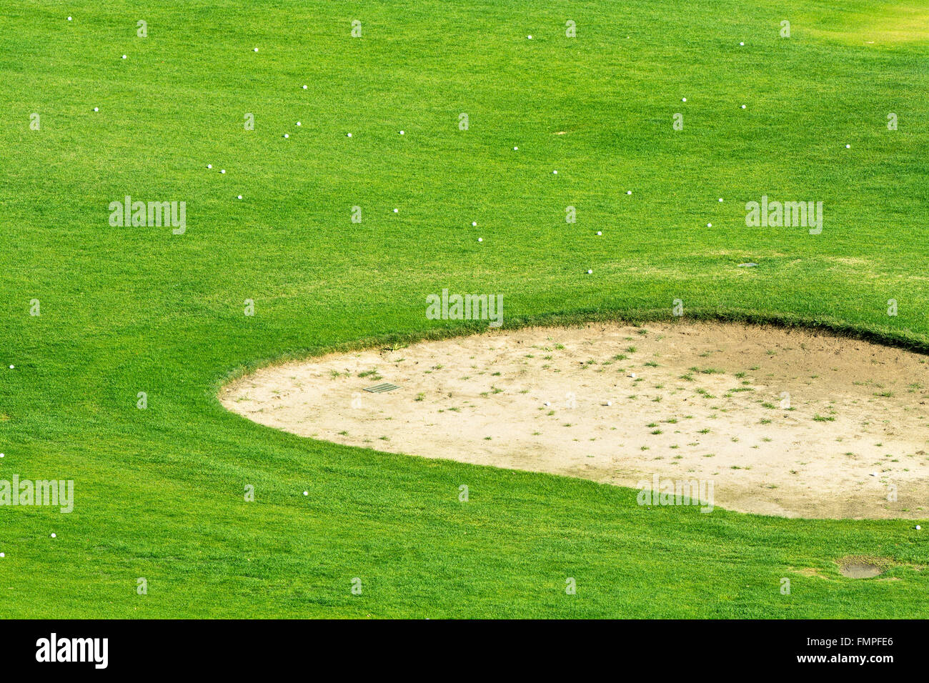 Close up of a golf course sand trap surrounded by golf balls during a sunny morning. Stock Photo