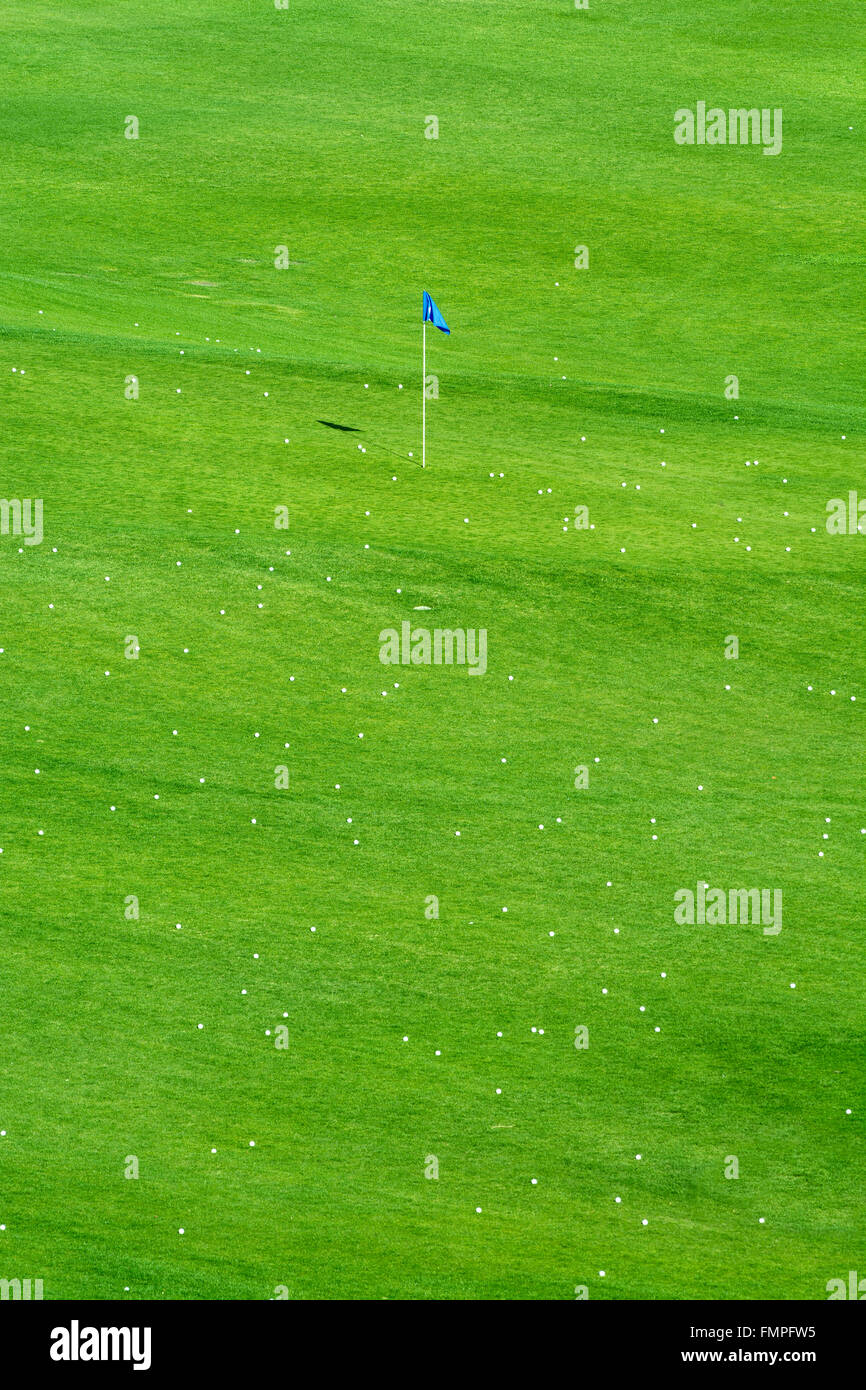 Early morning sunlight brings out the vibrant green colors of a golf course sprinkled with golf balls around a target flag Stock Photo