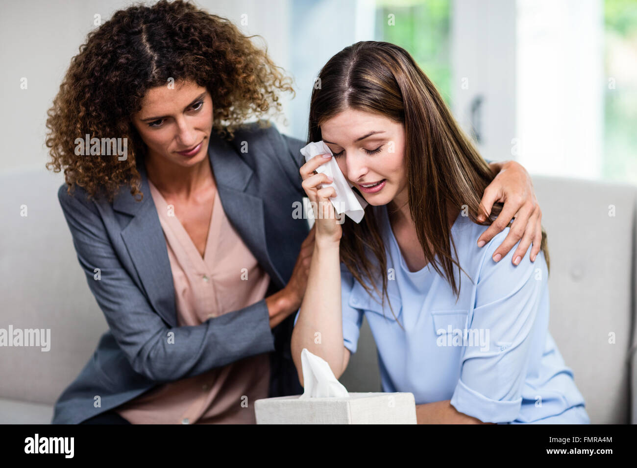 Female psychologist consoling depressed woman on sofa at home Stock Photo