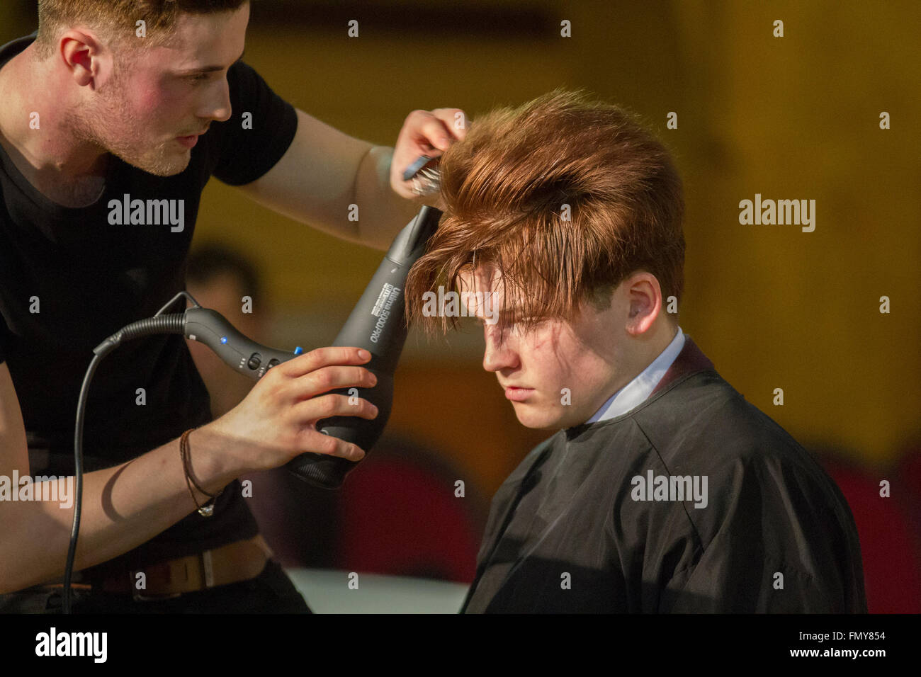 Male stylist blow drying hair in Blackpool March, 2016. Wintergardens Mens Hairdressing Competitions. Hair & Beauty NW is the North West's longest running major hair and beauty event, a venue for exciting competitions held by the National Hair Federation (N.H.F). The National Hairdressers' Federation is a trade industry group representing hairdressing salon owners in the United Kingdom. Stock Photo