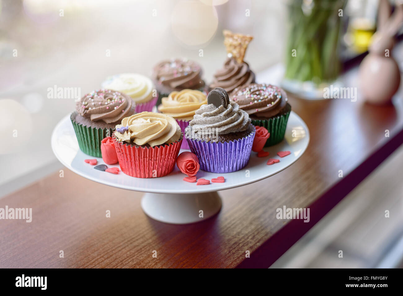 Eight deliciously sweet cupcakes covered with creamed chocolate, vanilla and various other garnishments alongside little pink he Stock Photo