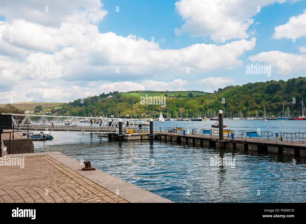 White clouds float in a blue sky above green countryside bordering the River Dart opposite the Dartmouth to Kingswear ferry port Stock Photo