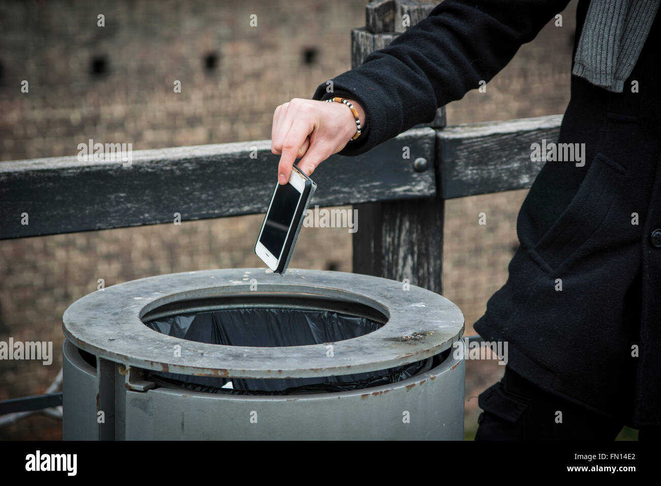 Unrecognizable man throwing his cell phone in trash bin in the street