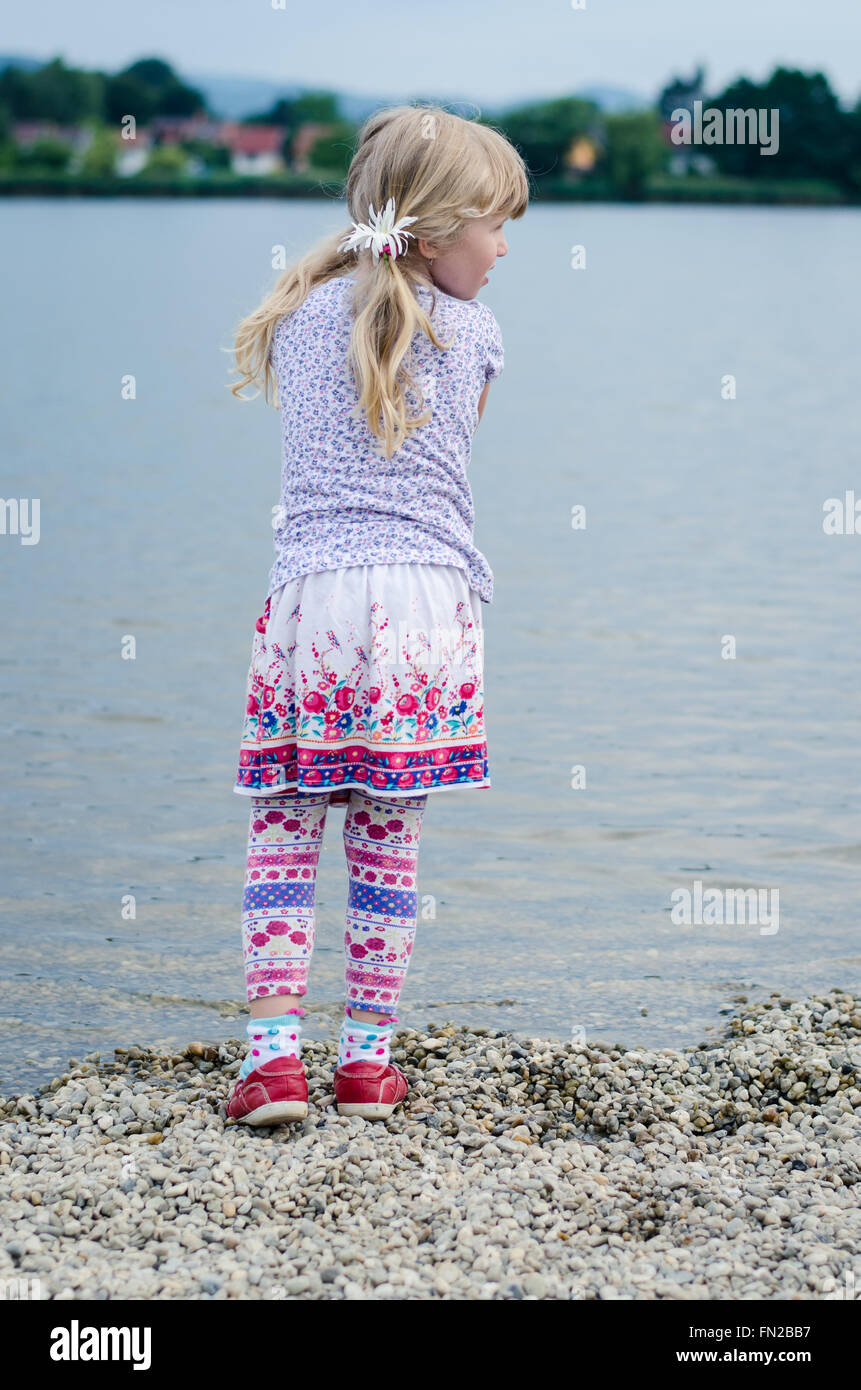 girl with long hair throwing stones into water back view Stock Photo