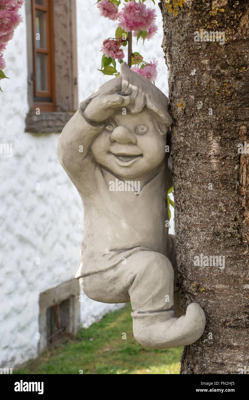 Funny little man of gray ceramic climbing at a tree in front of a house Stock Photo