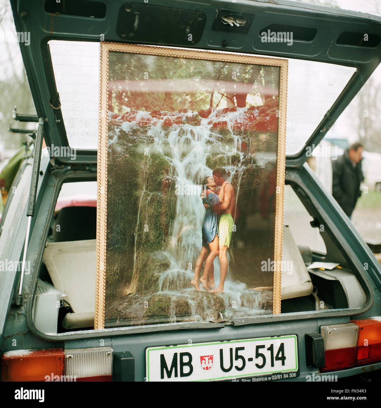 A photograph of a couple kissing in front a romantic waterfall, installed in the back of the car and being sold at flea market. Stock Photo