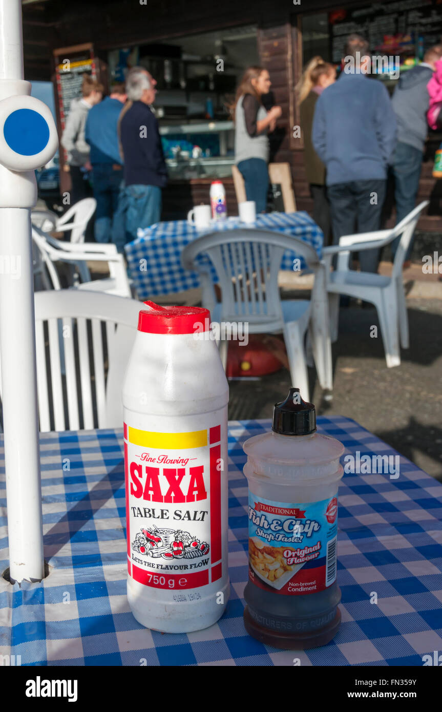 People queuing for fish & chips behind an outside table with salt and vinegar on it. Stock Photo