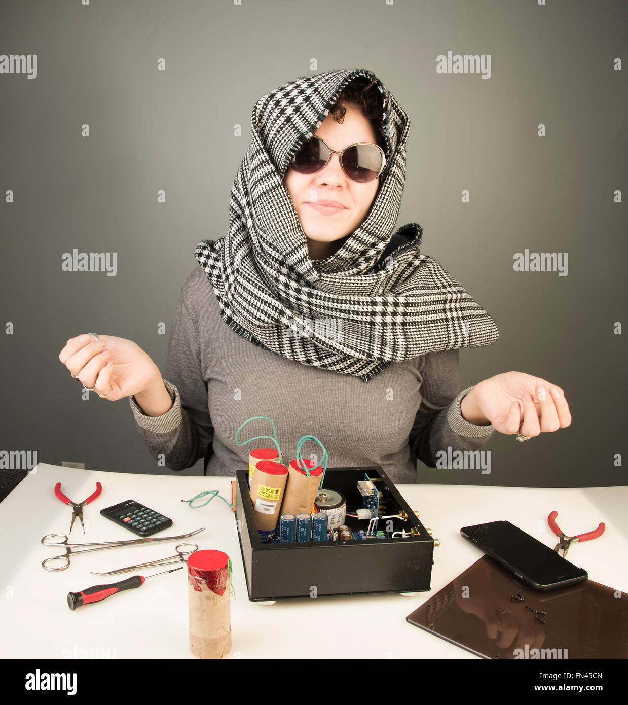 Danger Femme/Pretty stylish Caucasian woman wearing houndstooth headscarf sitting at table with components and explosives Stock Photo