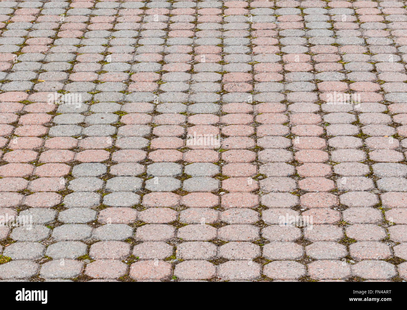 Octagonal pink and gray paving stones pattern in perspective with gravel and grass growing in spaces between stones. Stock Photo