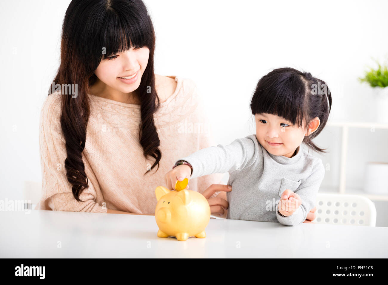 Happy mother and daughter Inserting Coin In Piggy bank Stock Photo - Alamy