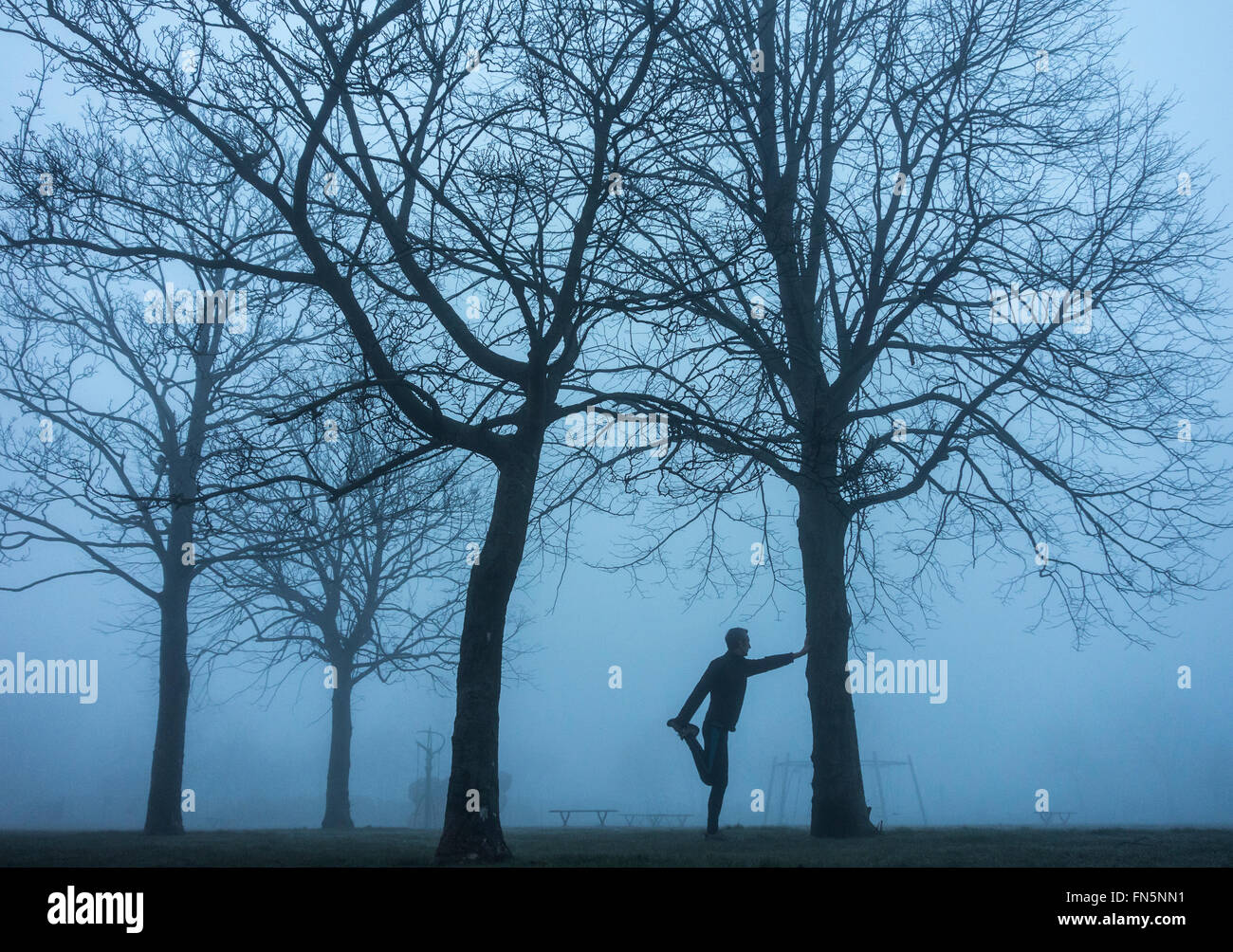 Billingham, north east England, UK, 14th March 2016. Weather: An almost monochrome Monday as a jogger stretches in Whitefield park in pre dawn light on a foggy Monday morning in Billingham, north east England. Credit:  Alan Dawson News/Alamy Live News Stock Photo