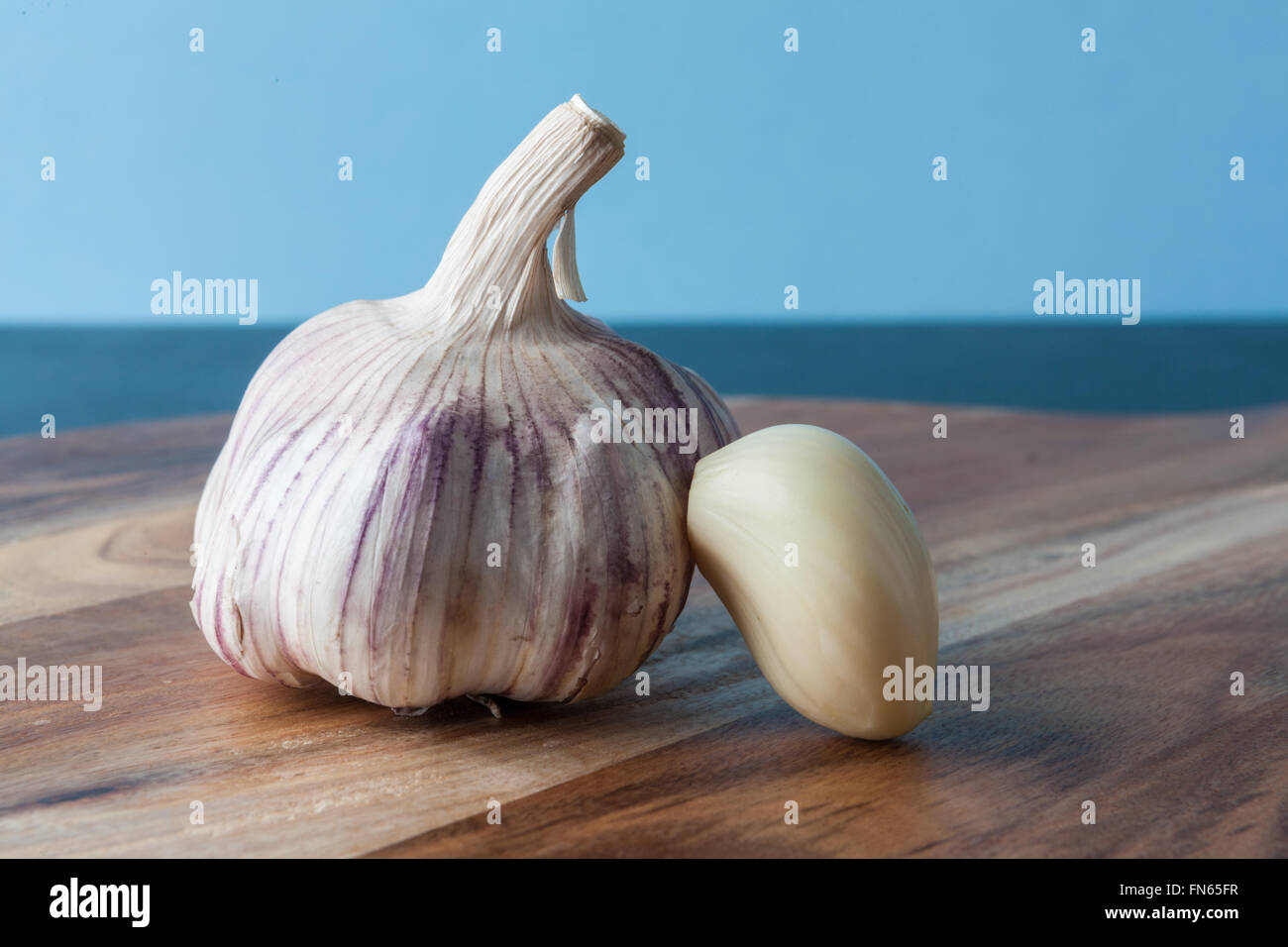 Closeup of peeled garlic clove and whole garlic on wooden chopping board with copy space. Stock Photo