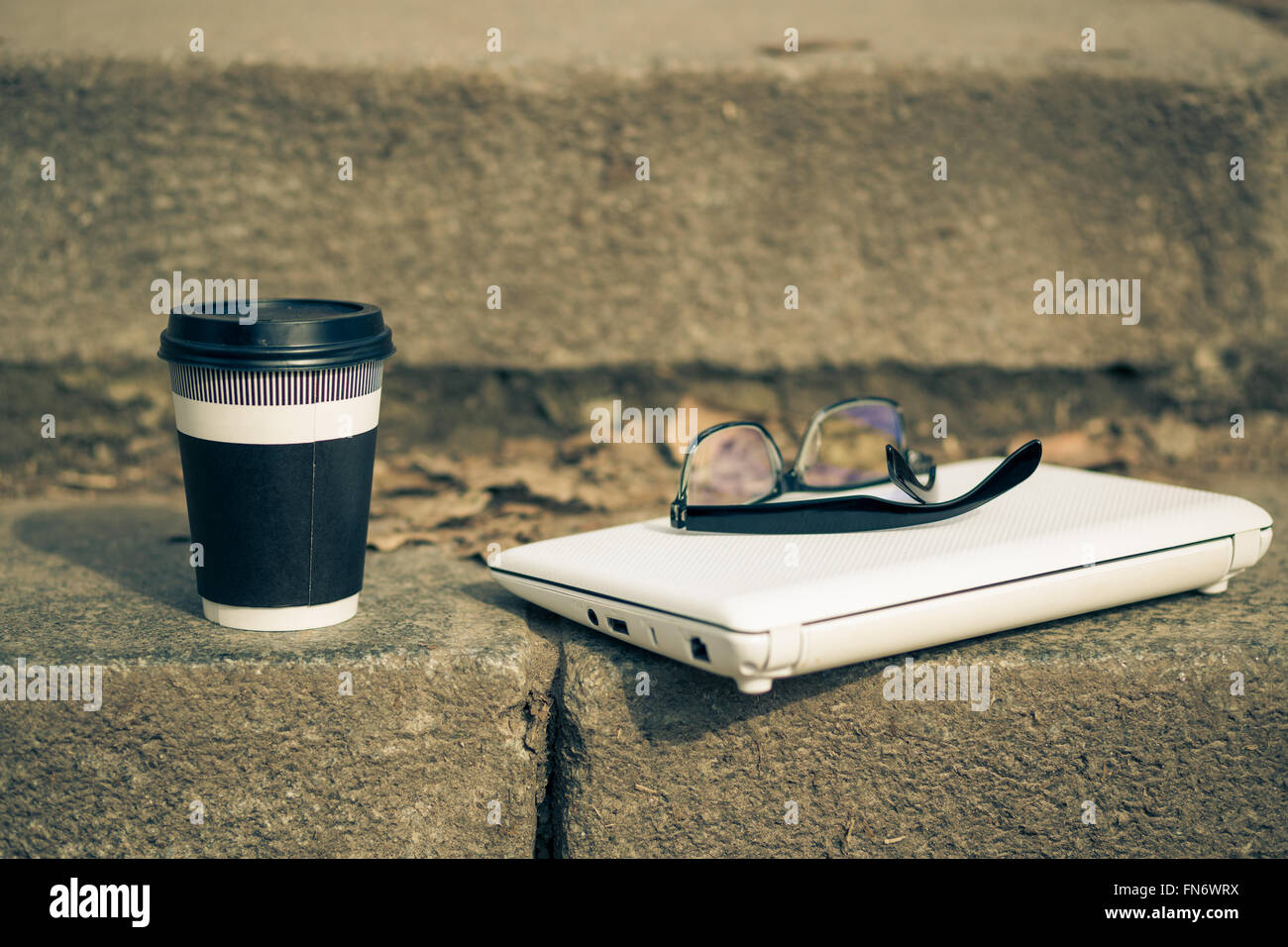 Mug of coffee with white laptop and protective glasses on the steps. Warm color toned image Stock Photo