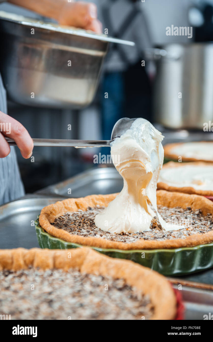 Chief cook in process of cooking several pies with cream on the kitchen Stock Photo
