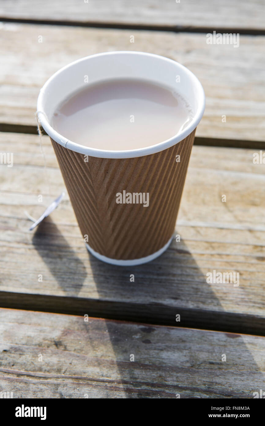 A throw away or recyclable paper cup of tea on a wodden table top in the sunshine. Stock Photo