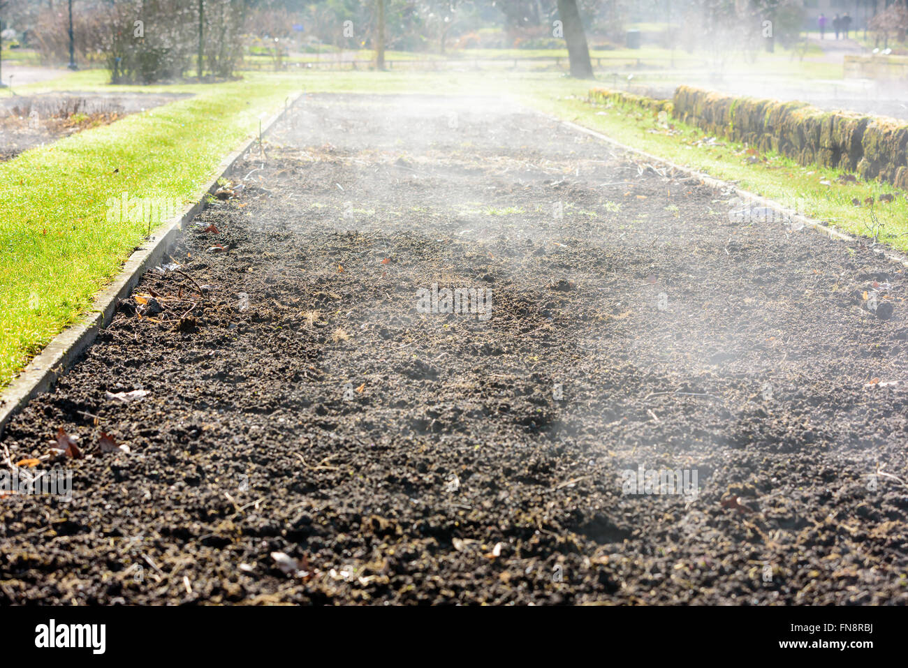 A rectangular flowerbed is getting warmed by the spring sunlight and gives of water vapor. Mist rises from the moist heated soil Stock Photo