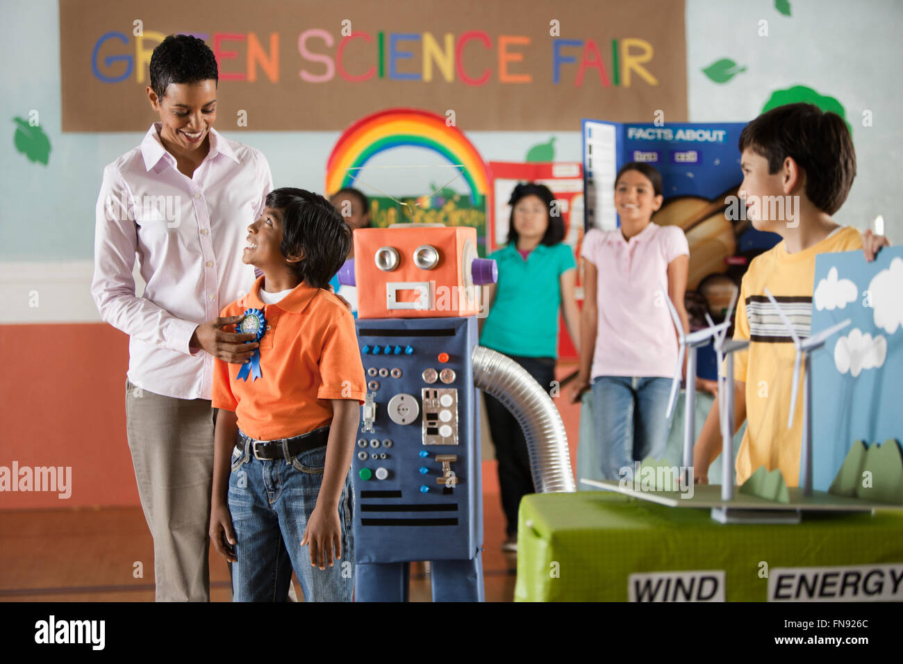A group of students and a teacher awarding a prize to a boy standing beside a robot model. Stock Photo