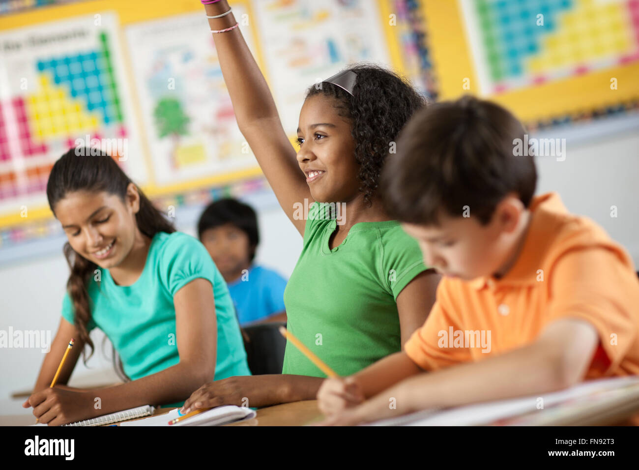 A group of young girls and boys in a classroom, classmates. A girl raising her hand. Stock Photo
